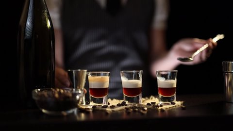 Bartender making B-52 cocktail, adding the final layer of brandy on top of coffee liqueur and Irish cream in shot glasses using cocktail spoon