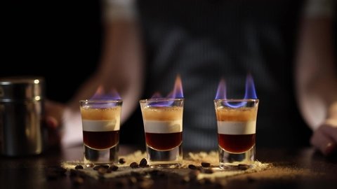 Bartender serving layered B52 cocktails on fire with sparkles caused by cinnamon powder sprinkles