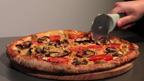 close up video- cutting a vegetarian tasty freshly made pizza with eggplant, sweet pepper, tomatoes, black and green olives, mushrooms rotating on a wooden plate