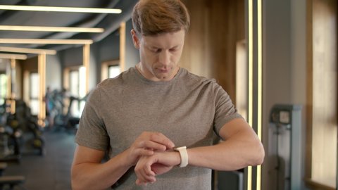 Portrait of confident bodybuilder using smart watch at gym. Closeup handsome sportsman checking results in fitness center. Serious fitness man looking at wrist watch in sport club.