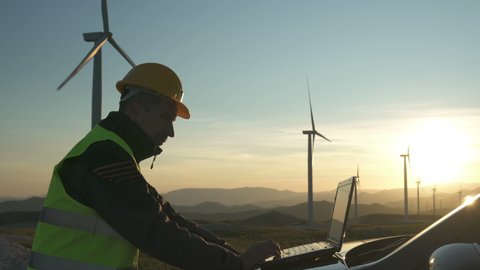 Technician Engineer in Wind Turbine Power Generator Station checks the status of the turbines using a laptop