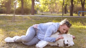 The girl lies on the grass with her dog, teasing, tickling her nose. White Samoyed sneezes. A woman loves a dog, love for pets, funny video.