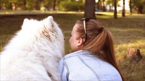 The girl lies on the grass with her dog, hugs. Beautiful white Samoyed. A woman loves a dog, love for pets, a walk in the park at sunset.