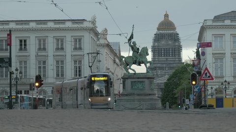 BRUSSELS/BELGIUM - APRIL 26TH 2019: Low angle shot of modern trams and buses passing each other on the Rue Royale in Brussels. The Statue of Godfrey of Bouillon and Palais de Justice on the background