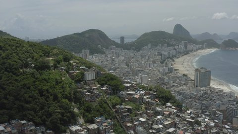 Aerial, panoramic footage of favelas on the hills of Rio de Janeiro with Copacabana in the background