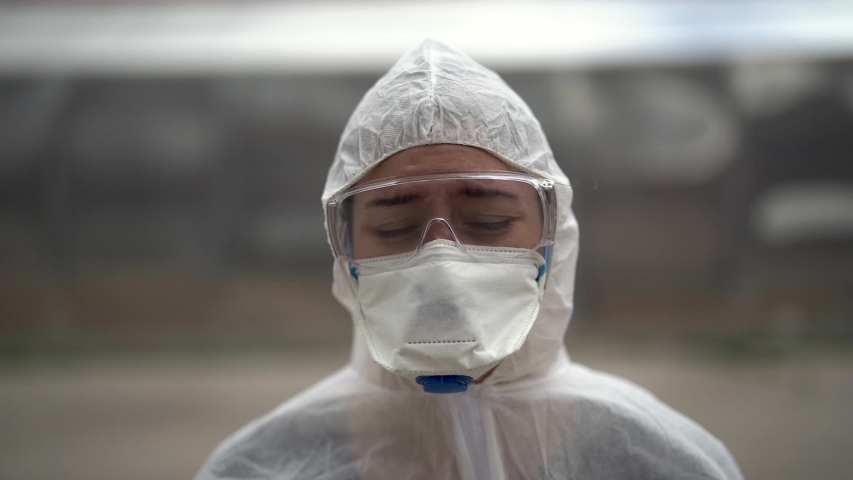 Exhausted crying doctor/nurse in coronavirus protective gear N95 mask.Covid-19 pandemic outbreak.Fatalities grief.Frontline worker mental stress,burnout.Face mask scars.Overworked healthcare provider	 | Shutterstock HD Video #1053409058