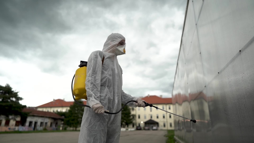 Disinfection specialist in private protective equipment (PPE) performing public decontamination.Hazmat suit virus protection. COVID-19 outbreak worker.Quarantined area.Dangerous hazard environment.	 | Shutterstock HD Video #1053409082