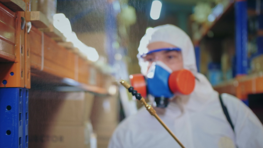 Man Disinfecting Warehouse. Covid-19. Corona Virus Disinfection. Antiseptic Sanitizer. Coronavirus Disinfectant. Worker Wear White Uniform Suit. Protect Mask. Spray Disinfecter. Covid 19 Sanitizing. Royalty-Free Stock Footage #1053409709