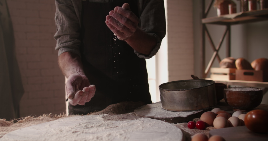 Experienced mature chef applying flour on hands before making traditional bread at bakery. Old man baking at home, enjoying hobby - closeup shot 4k footage | Shutterstock HD Video #1053414962