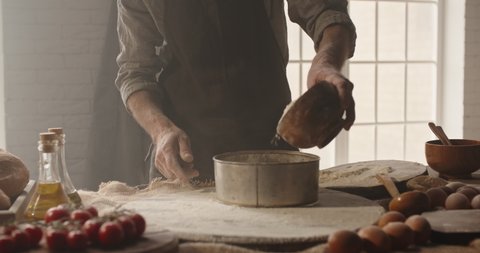 Closeup shot of hands of experienced chef working at bakery, sifting flour through sieve. Old man making traditional homemade bread - food and drink, hobby concept 4k footage