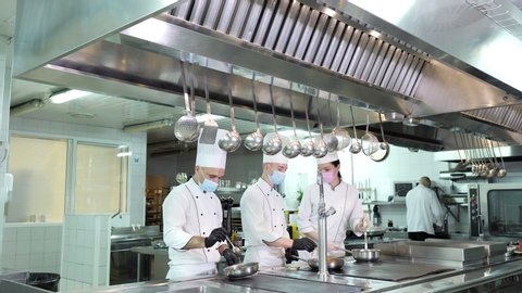 Chefs in protective masks and gloves prepare food in the kitchen of a restaurant or hotel