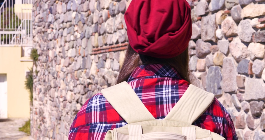 Young female traveler with backpack and red hat. Woman tourist walking at old european town. Hipster Girl traveler with backpack. Springtime or Summer in Europe. Travel and Vacation