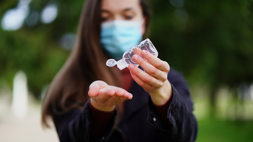Woman in medical protective mask applies antibacterial gel antiseptic to clean and disinfect hands outdoors | Shutterstock HD Video #1053420500