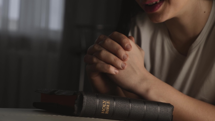 Woman prays with her hands crossed over Bible for God blessing in dark room. Faith and love in God.Christian prayer over Bible. Woman worshiping Christian God. Catholic faith.Girl prays in an epidemic | Shutterstock HD Video #1053425198