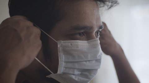 A close up shot of a young man or male wearing or putting protective face mask amid Corona virus or COVID 19 epidemic or pandemic