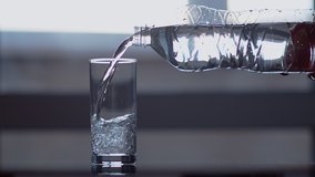 A man pours clear water from a plastic bottle into a glass, against the background of a window - Powered by Shutterstock - Get 15% off with code: PIKWIZARD15