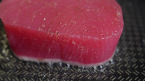 A piece of tuna is fried in oil in a frying pan