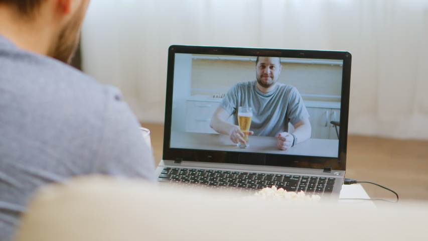 Back view of happy man on video call with his friend drinking beer during coronavirus isolation. Royalty-Free Stock Footage #1053429698