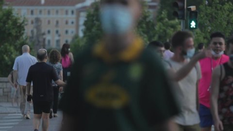 MADRID, SPAIN – May 29th 2020: Crowd of people (pedestrians) walking in a crosswalk wearing sanitary masks during the Coronavirus (Covid-19) pandemic. Spanish walking in the streets near a park.