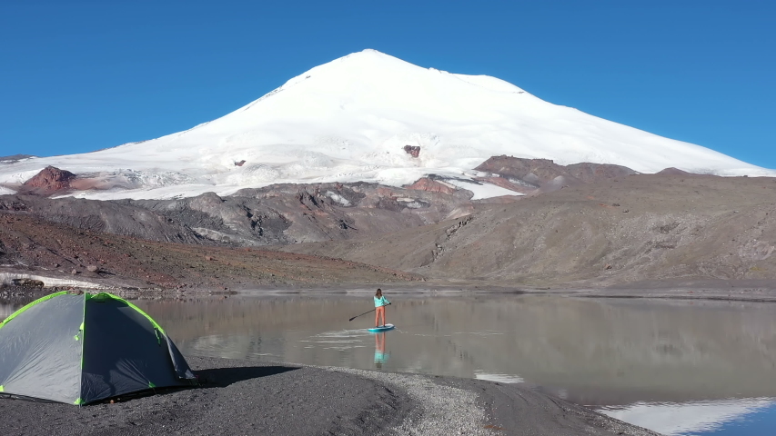 Woman Paddling on Stand Up Paddle Board on Mountain Lake 3300 Meters Above the Sea Level. Elbrus Mountain, Russia.