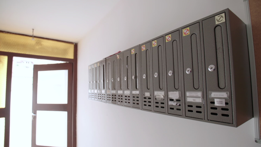 Socialistic old iron mail boxes. Dolly sliding over the post boxes in focus with blurred out names. Exit door from the building in the background.