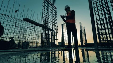 Builder checks his phone while standing on construction site.