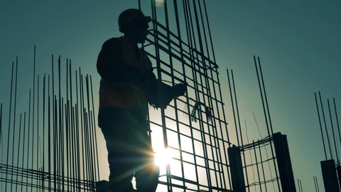 Construction worker works with armature on sunset background.
