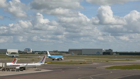 Amsterdam, May 22, 2015. A KLM plane taxiis to runway while another airplane in the background assumes speed as it is about to take off. Beautiful sky.