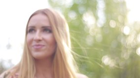 Video clip, blur effect and light fler, a young blonde woman with long hair in a long dress walks in a blossoming apple orchard on a sunny day in spring.