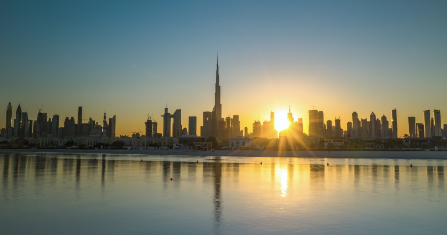 Sunrise in Dubai hyper lapse or time lapse view from boat or sea. The Sun rises over UAE skyscrapers at morning. Camera moves along beach, coast, shore