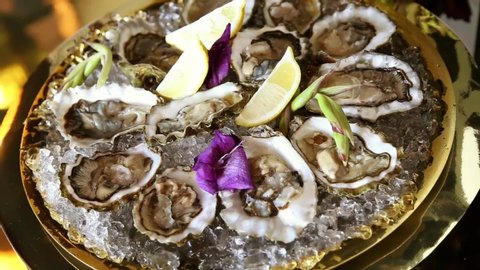 oysters in ice with lemon on a Golden platter with lilac gladioli petals