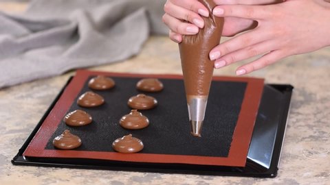 Cooking chocolate profiteroles, female hands squeeze the dough from the bag onto baking sheet.