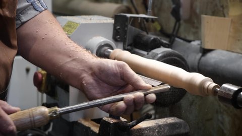 a man in a working apron works on a wood turning lathe. hands hold a chisel. hobby
