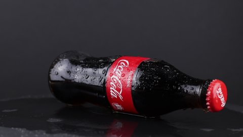 Minsk, Belarus, 05.2020 wet bottle with coca-cola rotating on the black background. cold glass is fogged up and water droplets running down. red classic logo of american company 
