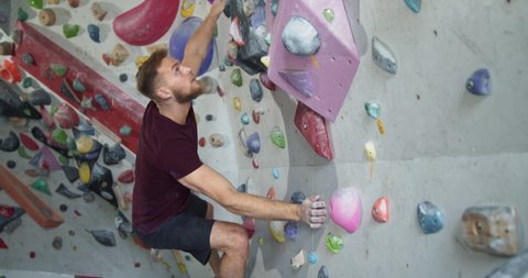Young bearded muscular athlete jumping on a climbing wall
