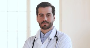 Happy young trustful medical worker doctor in white uniform with stethoscope looking at camera. head shot close up. Portrait of smiling handsome bearded professional general practitioner at workplace.