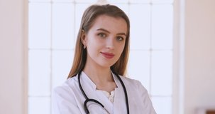 Close up head shot young attractive female doctor in white uniform with stethoscope looking at camera. Portrait of trustful skilled medical worker gp general practitioner standing in clinic office.