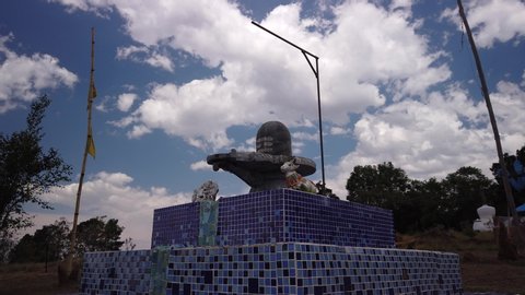 Wide angle time lapse of a Shiva Lingam statue, windy, clouds rushing away, light and shadow