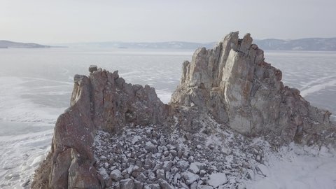 Aerial shot of Shamanka rock on Olkhon island in winter. Frozen lake Baikal in daylight, Siberia, Russia. Drone flies above mountain between rocks. Natural  snowy landscape.