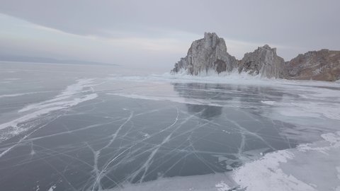 Aerial footage of Shamanka rock (mountain) ands Cape Burkhan on frozen Baikal lake on Olkhon island in winter. Russia. Beautiful snowy patterns on ice. Natural landscape of Siberia. Drone flies around