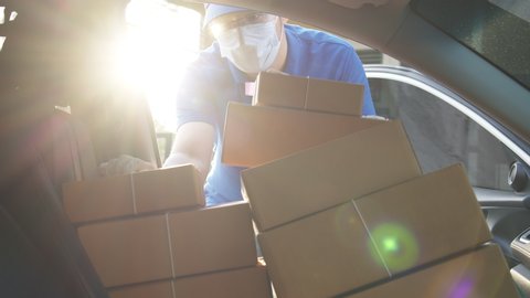 Asian volunteer delivery man or freelance re-arrange and deliver parcel paper box package in car at front house. Man in uniform, face mask and hand gloves for prevention coronavirus pandemic