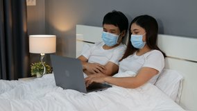 couple with medical masks using laptop on a bed during quarantine pandemic coronavirus(covid-19) stay at home. 4k video
