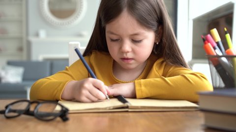 Cute smart primary school child girl learning writing doing homework sit at home table, adorable pretty little preschool kid studying alone making notes, children elementary education concept