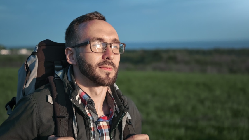 Happy backpacker guy in glasses smiling enjoying trekking at nature landscape steadicam establish shot. Smiling face of hiker male walking at sunset having positive emotion. 4k Dragon RED camera