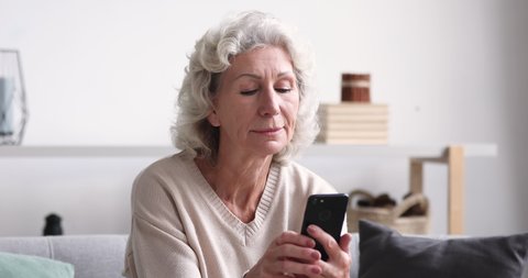 Head shot focused middle aged senior woman looking at smartphone screen, learning using mobile applications or software alone at home. Happy mature retired grandmother chatting with friends online.