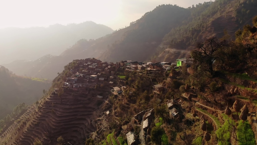 4k, Aerial view of Rural terrace farming  on a hilly landscape and Himalayan village of Uttarakhand, India, with mud Houses and cow shelters on a hill top. Drone view Royalty-Free Stock Footage #1053476276