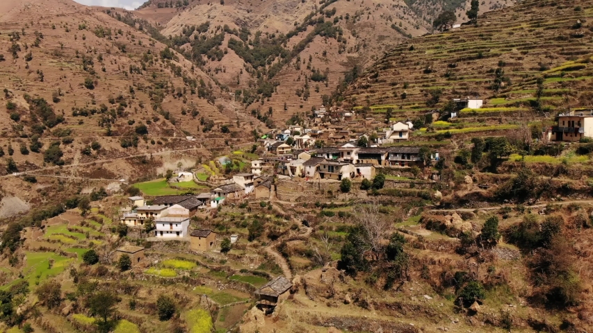 4k, Aerial view of Rural terrace farming on a hilly landscape and Himalayan village (Jhalpari) of Uttarakhand, India, with mud Houses and cow shelters on a hilltop. Drone view of dense Forest Royalty-Free Stock Footage #1053476318