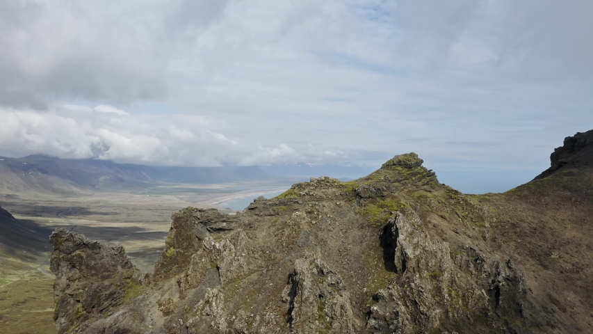Aerial drone shot flying towards high mountain peak hidden in clouds. View from sky over rocky landscape full of rocks, stones and ocean in background. Adventurous trek in Snaefellsnes area, Iceland