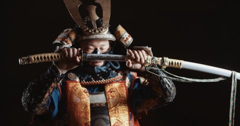 Man in traditional japanese samurai clothing is looking at camera and demontrating his katana sword, isolated on black background - culture, tradition, martial arts concept 4k footage