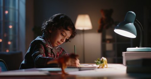 Funny little asian kid drawing at home. Boy with curly hair using his imagination, creating art in evening at home, dreaming of becoming artist - childhood dream, hobby concept 4k footage